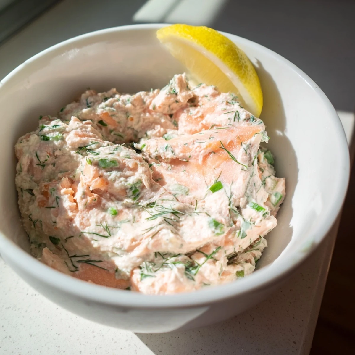 A bowl of creamy Smoked Salmon Dip garnished with fresh dill and lemon wedges, ready for dipping.