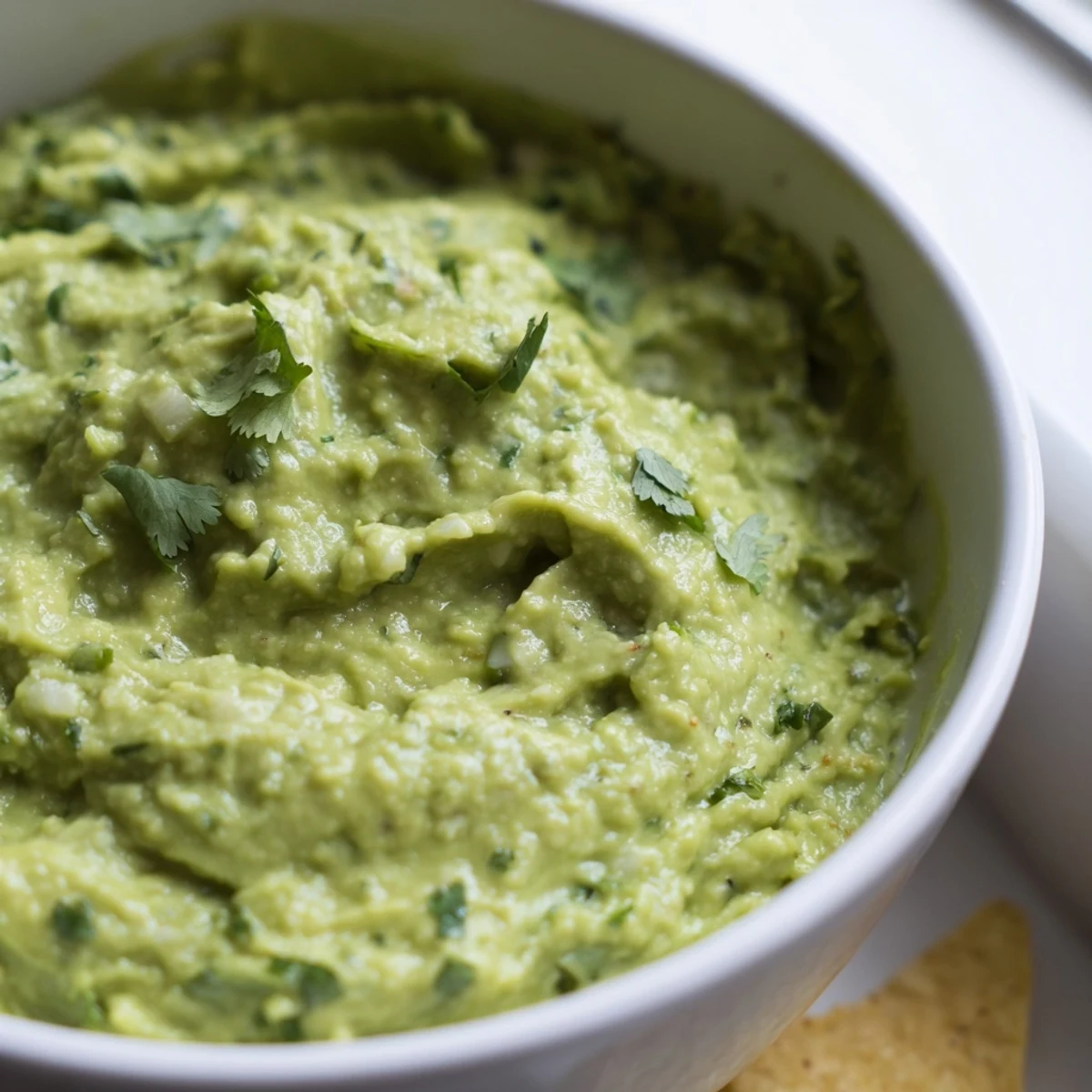 Vibrant avocado lime dip in a white bowl with lime wedges and crisp corn chips, ready for a party platter.