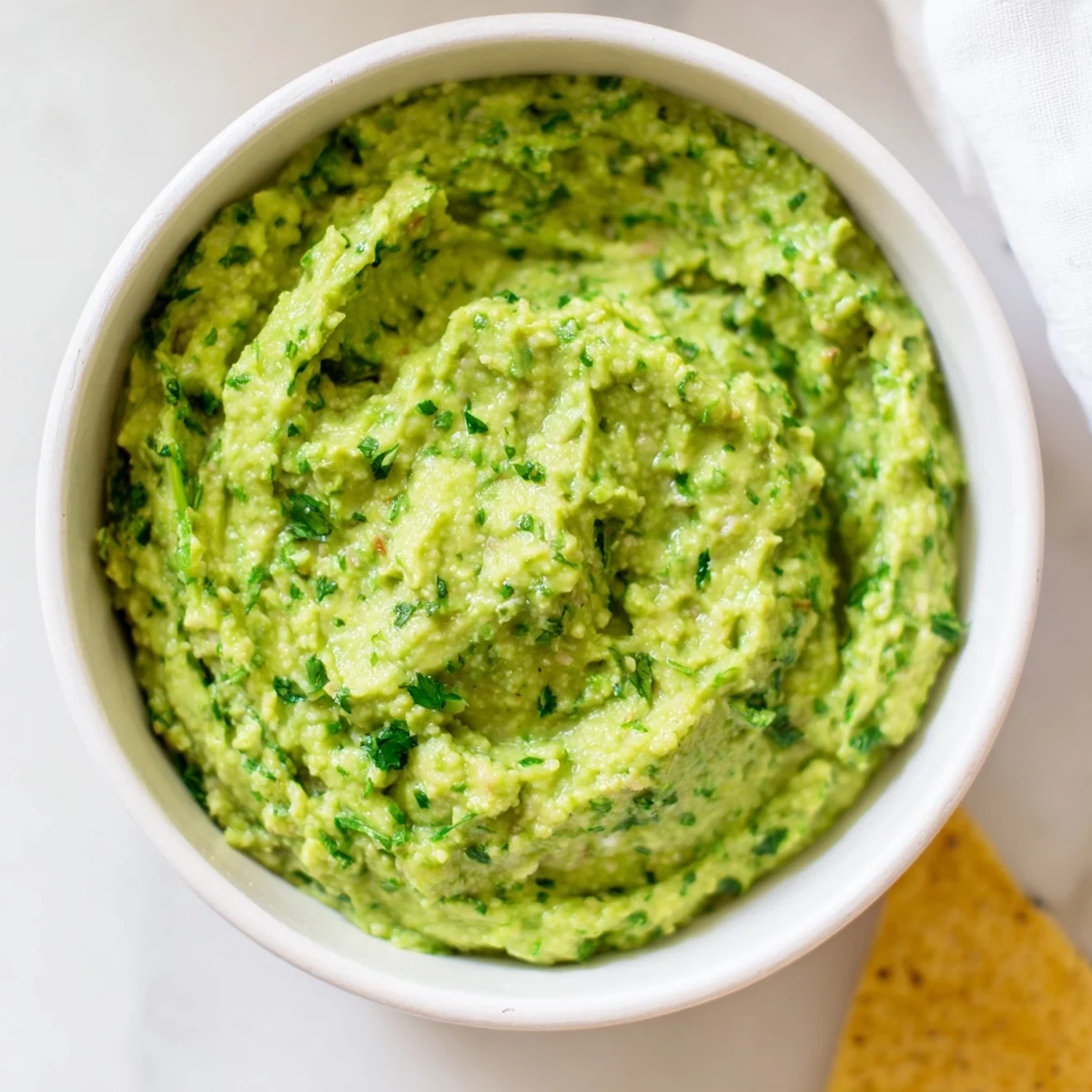 Bright green avocado lime dip topped with fresh cilantro and jalapeño slices, alongside colorful vegetable sticks for dipping.