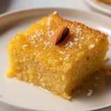 A close-up of warm, delicious Egyptian Basbousa, showcasing coconut flakes and a glistening syrup glaze.