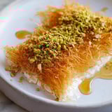 A close-up of crispy, buttery shredded phyllo around a warm, cheesy Knafeh.