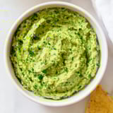 Bright green avocado lime dip topped with fresh cilantro and jalapeño slices, alongside colorful vegetable sticks for dipping.