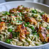 Creamy one-pot lemon orzo with chicken and peas, served steaming hot in a rustic skillet with lemon wedges and fresh parsley.