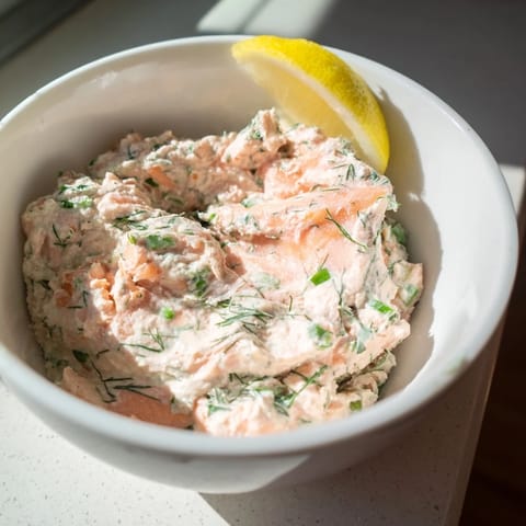 A bowl of creamy Smoked Salmon Dip garnished with fresh dill and lemon wedges, ready for dipping.