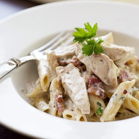 A hearty bowl of Creamy Chicken Bacon Penne topped with fresh parsley and extra Parmesan cheese, fork-ready.