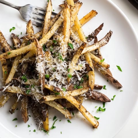 A close-up of rustic Truffle Parmesan Fries in a serving basket, paired with creamy garlic aioli for dipping.