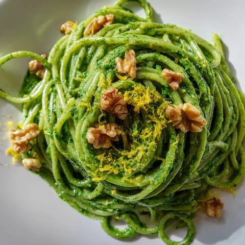 A bowl of Creamy Spinach Walnut Pasta twirled on a fork, showing the velvety green sauce and spinach flecks.