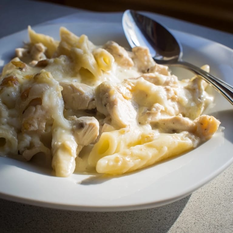 A close-up of baked chicken Alfredo casserole in a white dish, garnished with fresh parsley and ready to serve.