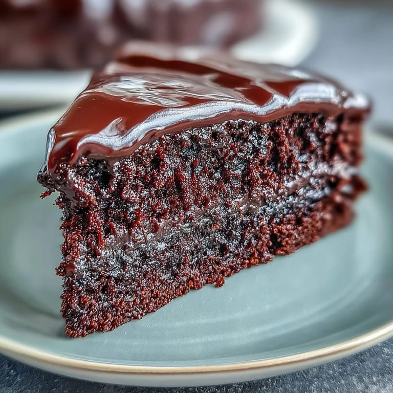 Moist, squidgy Easy Chocolate Fudge Cake layers with silky chocolate icing on a rustic cake stand.